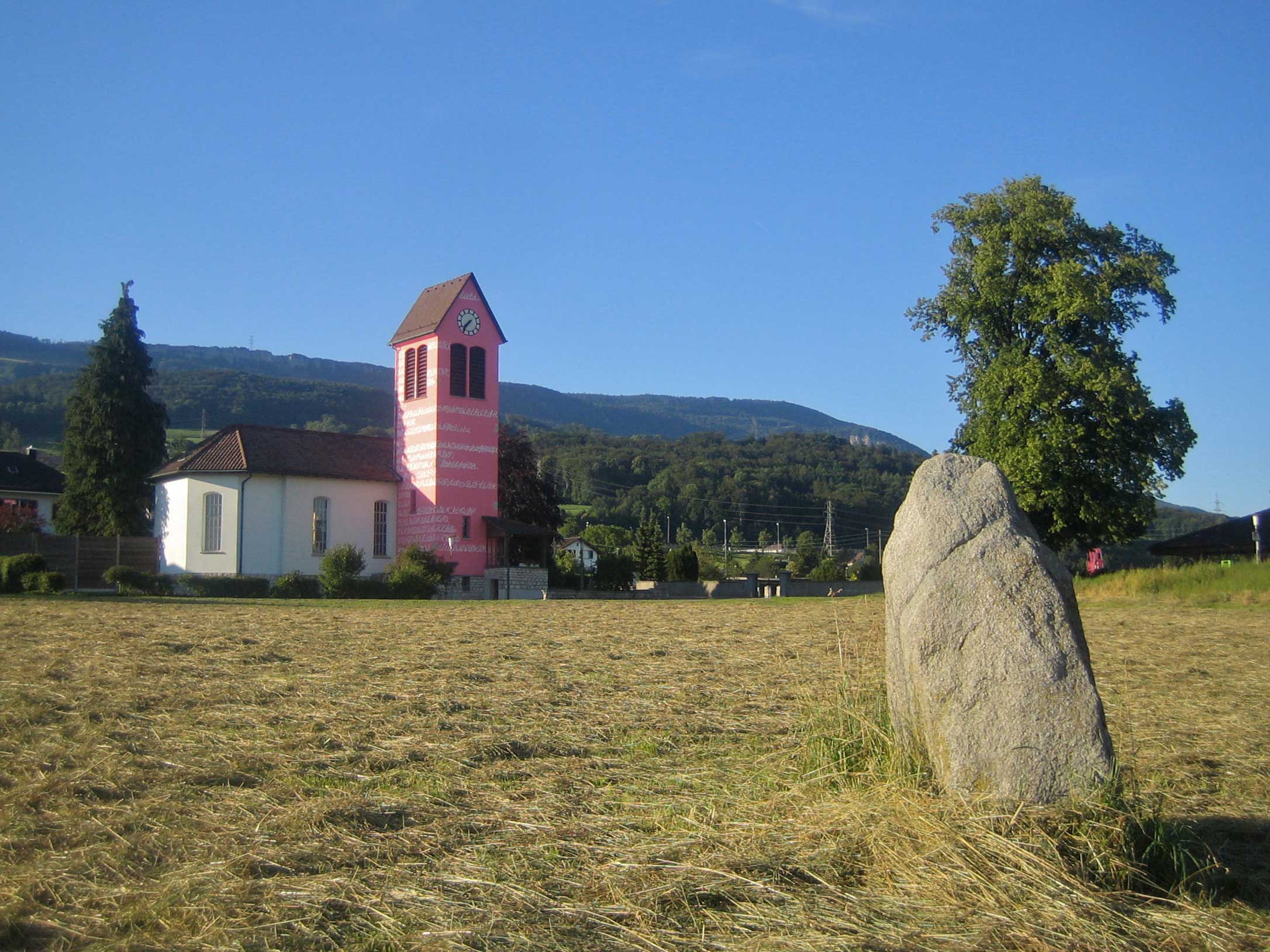 Attiswil: Freistein von Südwesten mit rosaroter Kirche (Kulturweg Kulturundum)